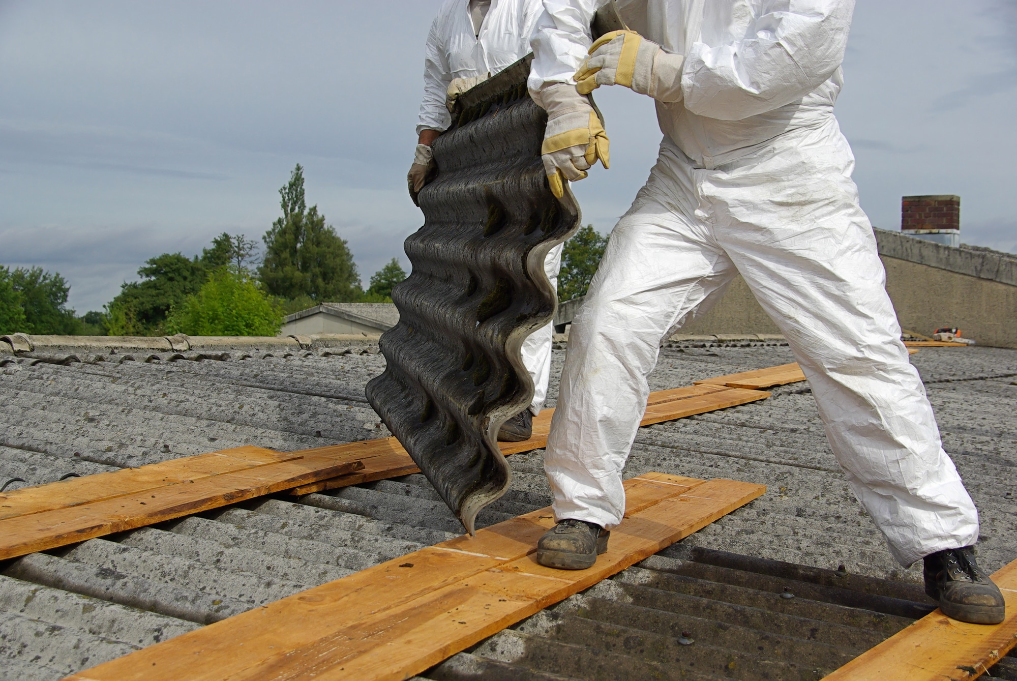 Two men standing on wooden planks carrying asbestos